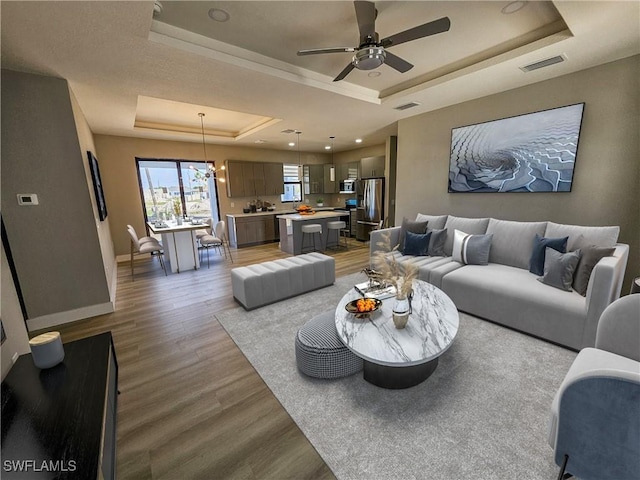 living room with hardwood / wood-style floors, ceiling fan with notable chandelier, and a tray ceiling