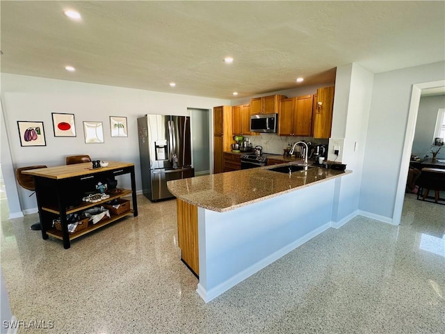 kitchen featuring sink, stainless steel appliances, tasteful backsplash, kitchen peninsula, and dark stone countertops