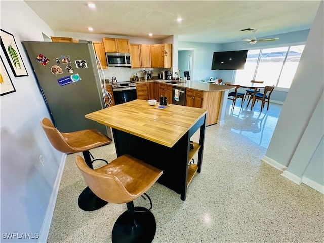 kitchen with ceiling fan, stainless steel appliances, a kitchen breakfast bar, backsplash, and kitchen peninsula