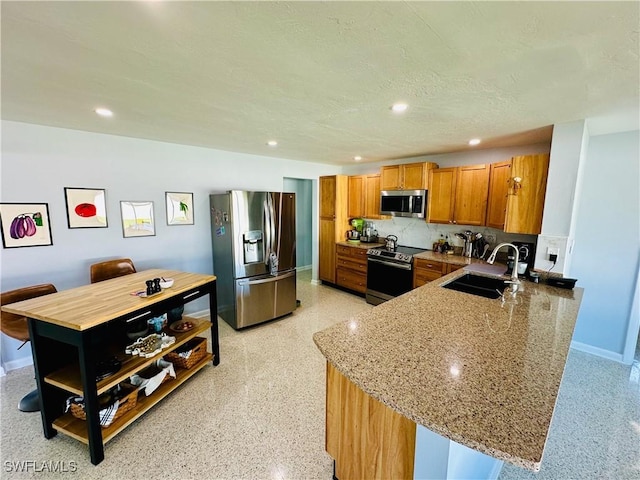 kitchen with sink, stainless steel appliances, light stone counters, kitchen peninsula, and decorative backsplash