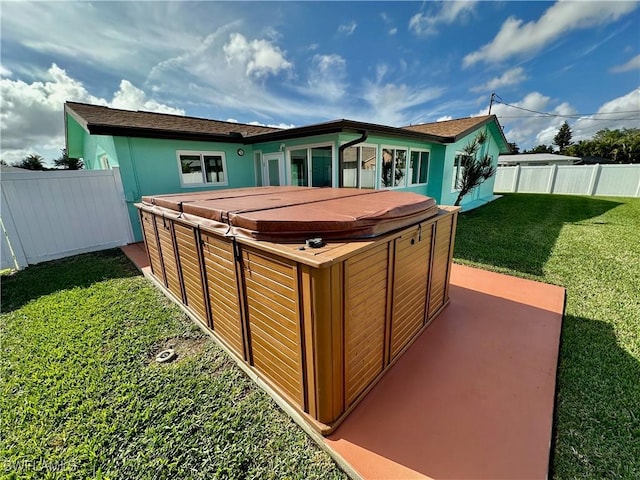 rear view of property featuring a patio, a hot tub, and a lawn