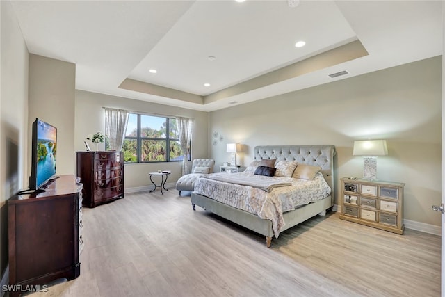 bedroom with a raised ceiling and light wood-type flooring