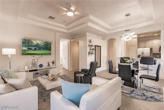 living room with a tray ceiling, ceiling fan, and light tile patterned floors