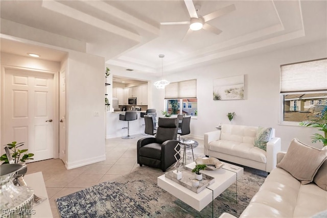 tiled living room featuring a tray ceiling and ceiling fan with notable chandelier