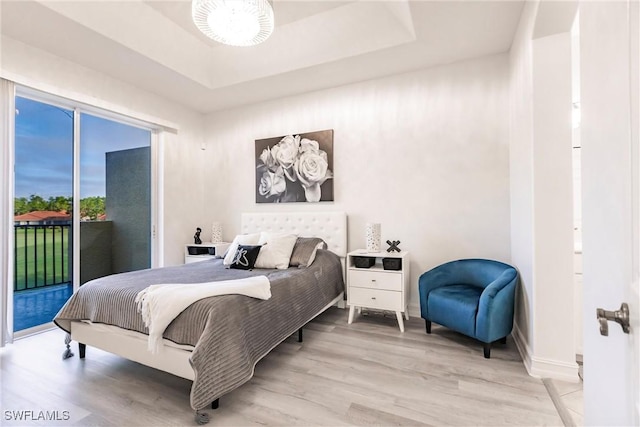 bedroom with light wood-type flooring, access to outside, and a tray ceiling