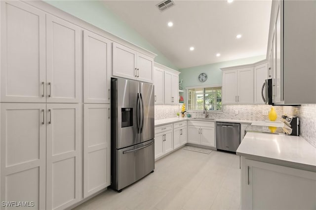 kitchen with white cabinetry, backsplash, appliances with stainless steel finishes, and vaulted ceiling