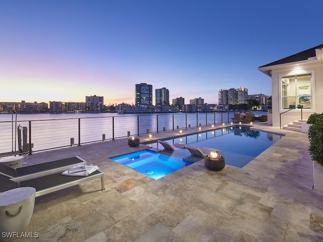 pool at dusk featuring an in ground hot tub, a water view, and a patio area