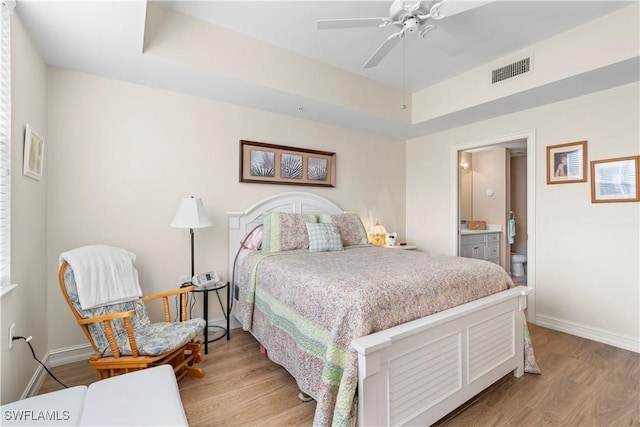 bedroom with a raised ceiling, ensuite bath, ceiling fan, and light wood-type flooring