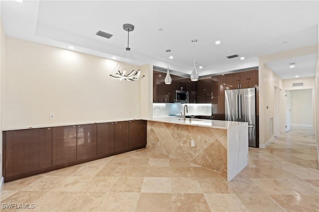 kitchen featuring kitchen peninsula, stainless steel appliances, sink, pendant lighting, and an inviting chandelier