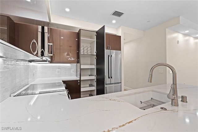 kitchen with sink, light stone counters, decorative backsplash, dark brown cabinets, and appliances with stainless steel finishes