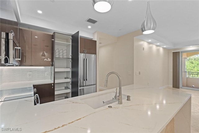 kitchen with sink, hanging light fixtures, decorative backsplash, light stone countertops, and appliances with stainless steel finishes