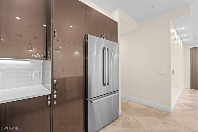 kitchen with stainless steel refrigerator, decorative backsplash, dark brown cabinetry, and light stone countertops