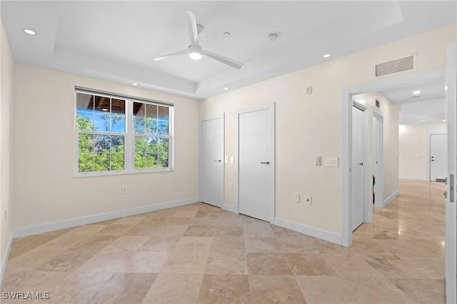 unfurnished bedroom featuring a tray ceiling, ceiling fan, and two closets