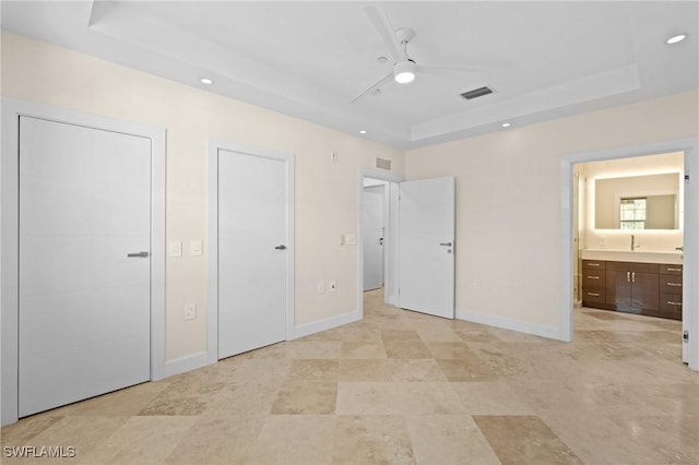 unfurnished bedroom featuring ceiling fan, ensuite bathroom, and a tray ceiling