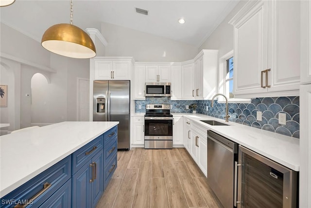 kitchen with blue cabinetry, beverage cooler, stainless steel appliances, pendant lighting, and vaulted ceiling