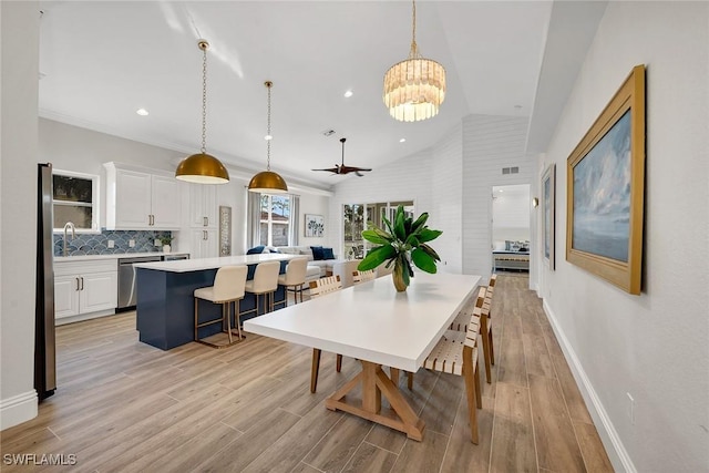 dining room with ceiling fan with notable chandelier, light hardwood / wood-style flooring, and vaulted ceiling