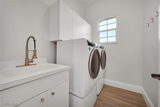 washroom with cabinets, light wood-type flooring, washer and clothes dryer, and sink