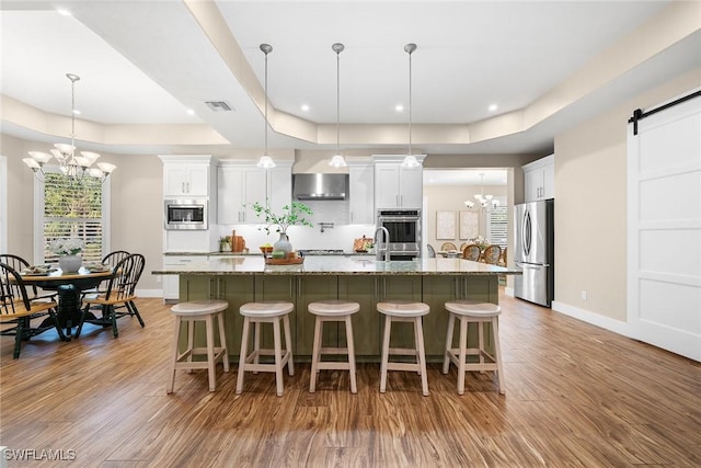 kitchen with white cabinetry, stainless steel appliances, a barn door, light stone counters, and light hardwood / wood-style floors