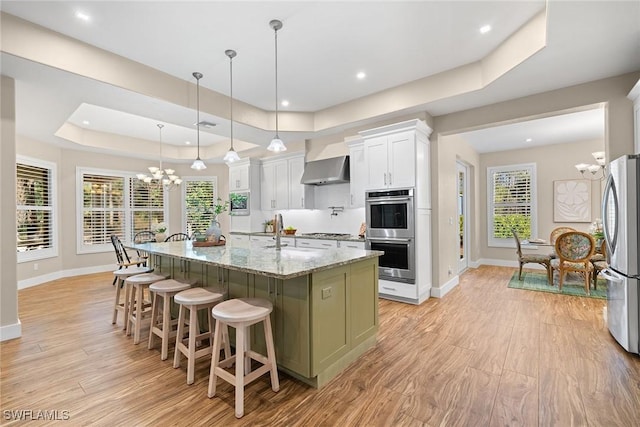 kitchen featuring light stone countertops, appliances with stainless steel finishes, pendant lighting, a center island with sink, and white cabinets