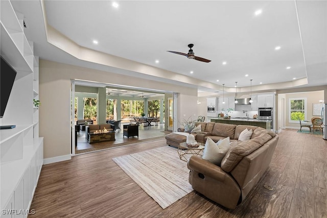 living room featuring hardwood / wood-style flooring, a raised ceiling, ceiling fan, and sink