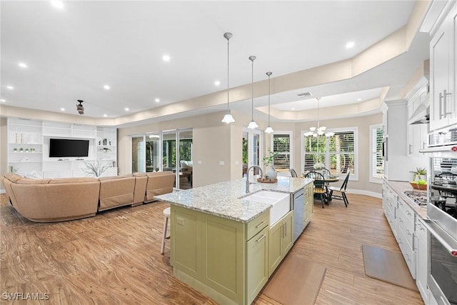 kitchen with decorative light fixtures, a center island with sink, green cabinetry, white cabinets, and light hardwood / wood-style floors