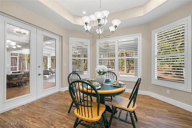 dining space with a tray ceiling, hardwood / wood-style floors, french doors, and a notable chandelier