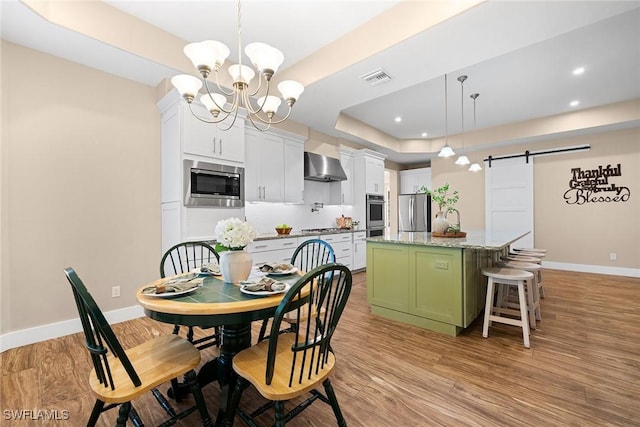 kitchen with stainless steel appliances, wall chimney range hood, a barn door, white cabinets, and a center island