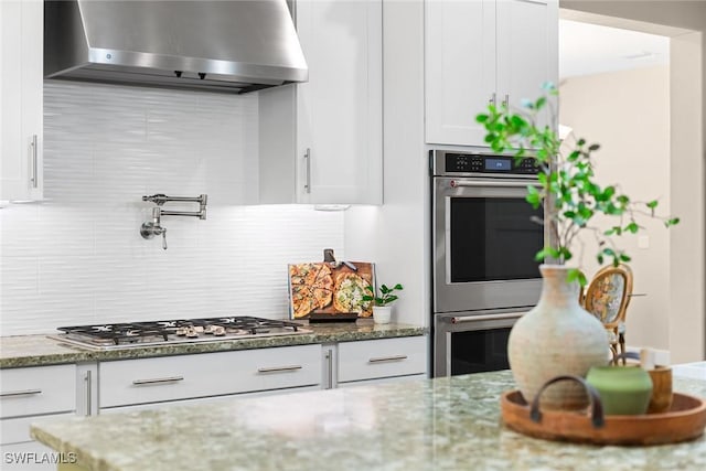 kitchen featuring appliances with stainless steel finishes, white cabinetry, extractor fan, and dark stone counters