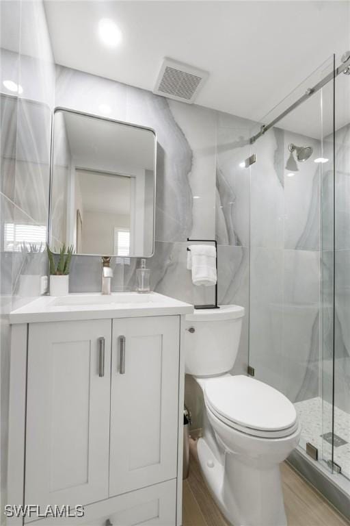 bathroom featuring an enclosed shower, vanity, wood-type flooring, tile walls, and toilet