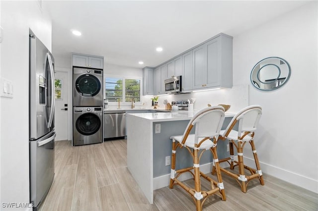 kitchen featuring stacked washer and dryer, light countertops, appliances with stainless steel finishes, a peninsula, and a kitchen bar