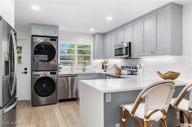 kitchen with a peninsula, stainless steel appliances, light countertops, stacked washing maching and dryer, and a kitchen bar