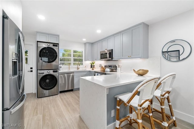 kitchen featuring sink, appliances with stainless steel finishes, stacked washer / drying machine, kitchen peninsula, and a breakfast bar area