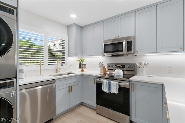 kitchen featuring gray cabinets, sink, stainless steel appliances, and stacked washer and clothes dryer