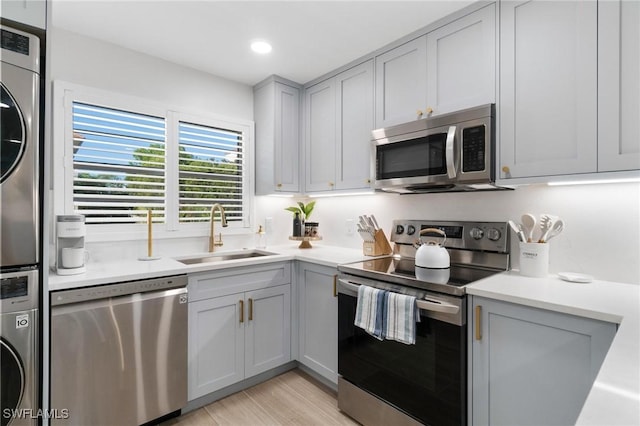 kitchen featuring stacked washer and dryer, sink, gray cabinets, appliances with stainless steel finishes, and light hardwood / wood-style floors