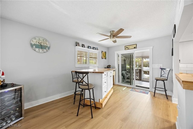 kitchen with a kitchen breakfast bar, light hardwood / wood-style flooring, ceiling fan, white cabinetry, and butcher block counters