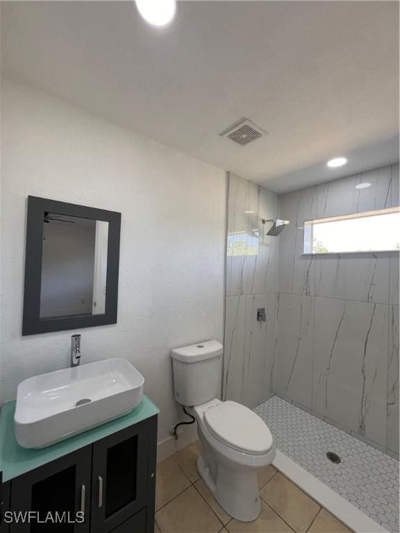 bathroom featuring tile patterned flooring, vanity, toilet, and tiled shower