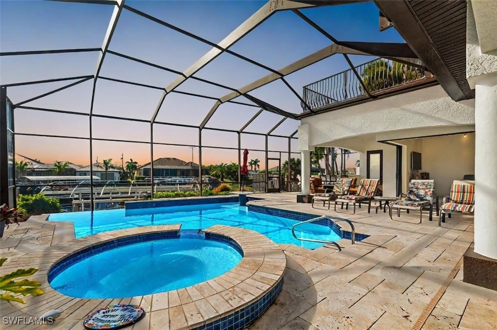 pool at dusk with glass enclosure, a patio area, and an in ground hot tub