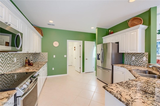 kitchen with sink, stainless steel appliances, light tile patterned floors, light stone counters, and white cabinets