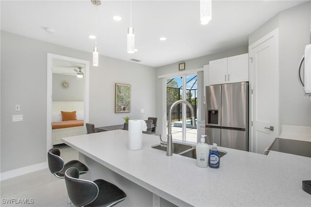 kitchen featuring a breakfast bar, stainless steel refrigerator with ice dispenser, hanging light fixtures, ceiling fan, and white cabinetry