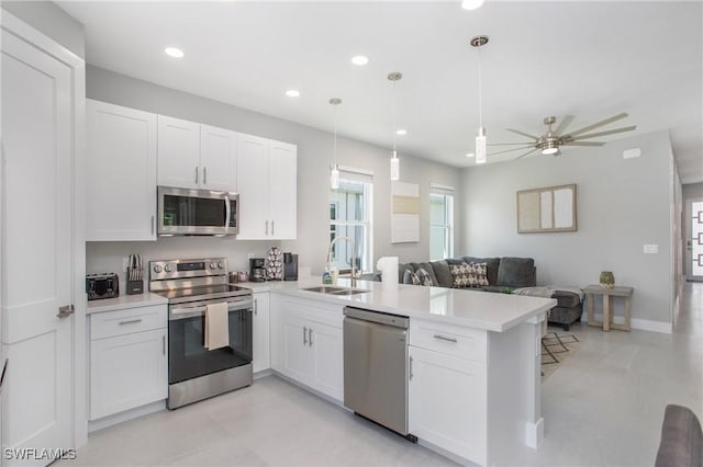 kitchen with sink, kitchen peninsula, pendant lighting, white cabinets, and appliances with stainless steel finishes