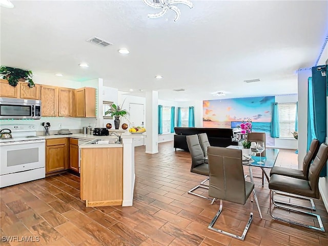 kitchen with white range with electric cooktop, wood-type flooring, sink, a kitchen bar, and kitchen peninsula