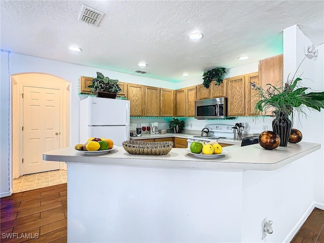 kitchen with kitchen peninsula, dark hardwood / wood-style flooring, white appliances, and a textured ceiling