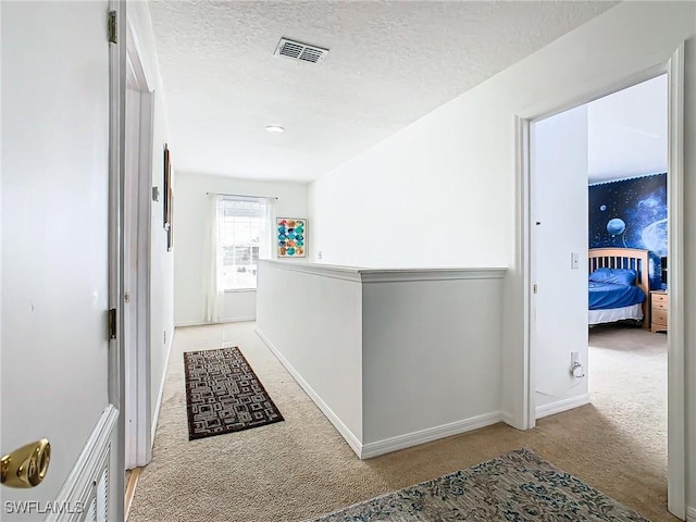 hall with a textured ceiling and light colored carpet