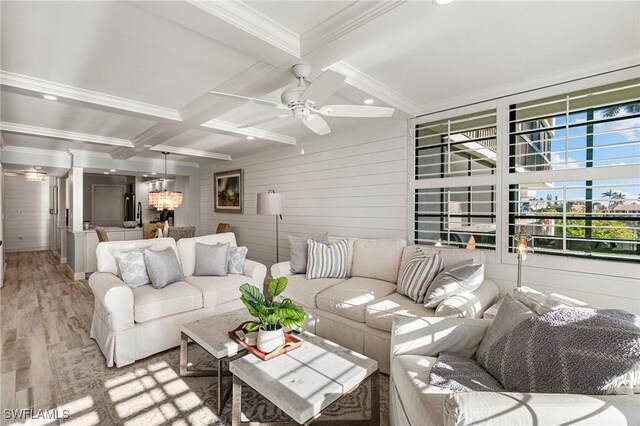 living room with wood walls, coffered ceiling, ceiling fan with notable chandelier, beamed ceiling, and light hardwood / wood-style floors