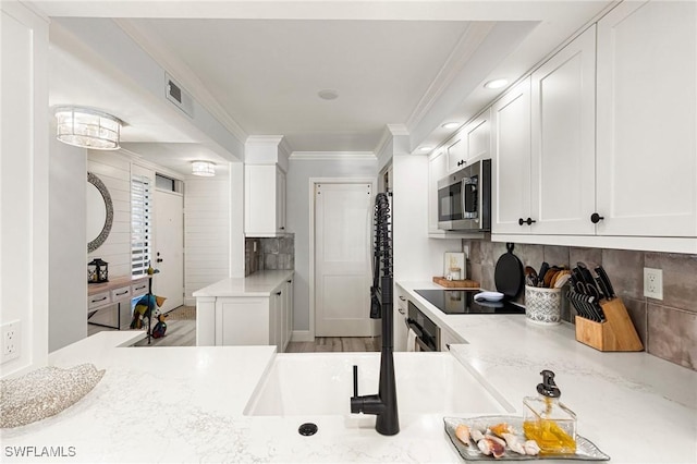 kitchen with kitchen peninsula, decorative backsplash, white cabinets, black appliances, and ornamental molding