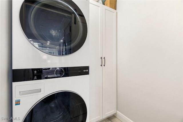 clothes washing area with cabinets and stacked washer / drying machine