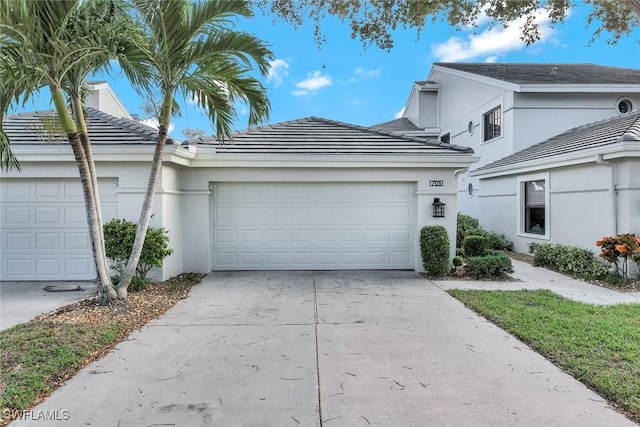 view of front facade featuring a tile roof, driveway, an attached garage, and stucco siding