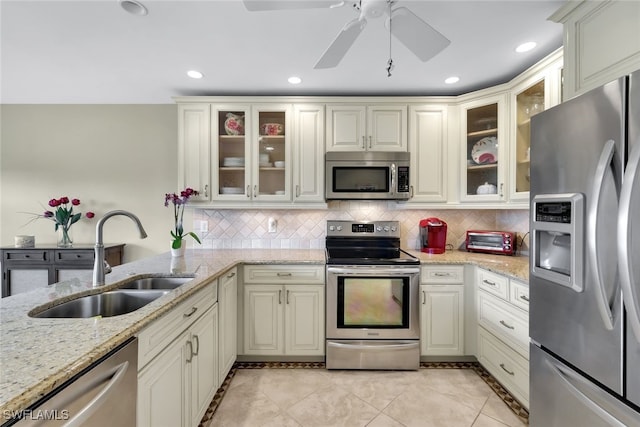 kitchen with light stone counters, a sink, appliances with stainless steel finishes, decorative backsplash, and glass insert cabinets