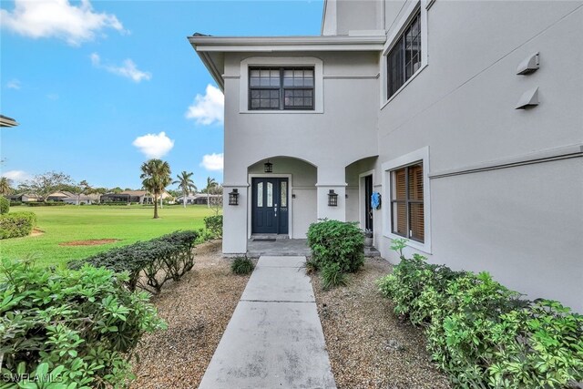 view of exterior entry with a lawn and stucco siding