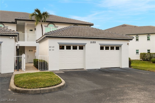 view of front facade with a balcony, a garage, driveway, a tiled roof, and stucco siding